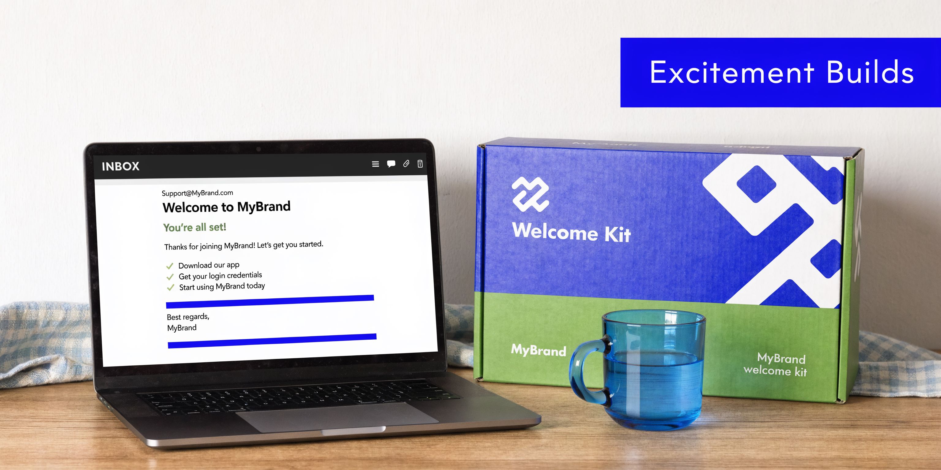 A laptop showing a welcome email from MyBrand sitting next to a branded welcome kit and mug.