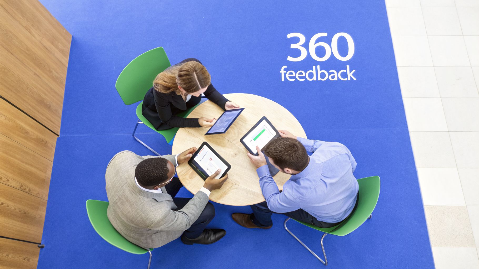 Three professionals review 360 feedback on tablets, highlighting digital performance evaluation.