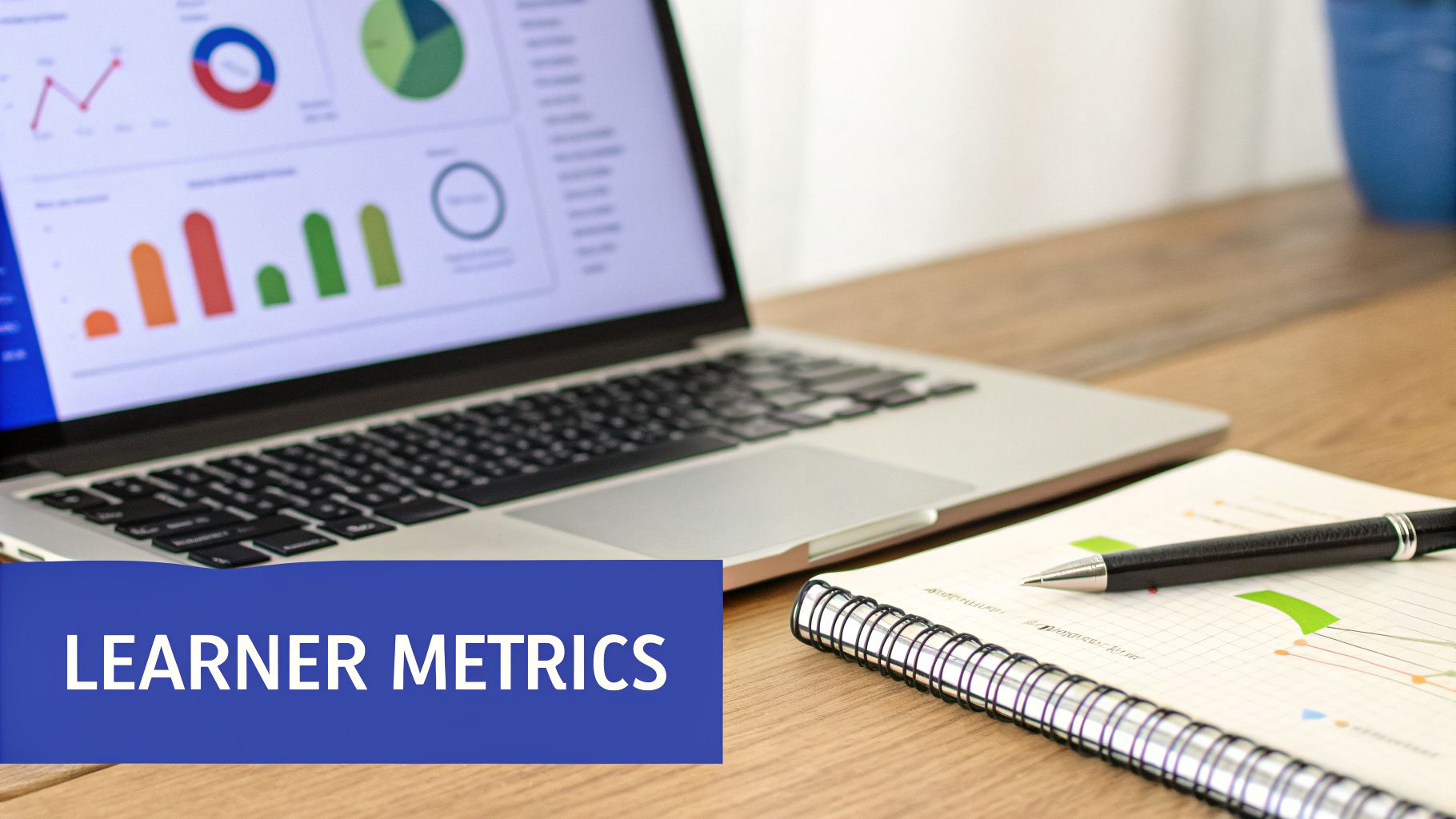 Laptop screen with colorful business graphs and charts, next to a notebook with a pen, labeled 'LEARNER METRICS'.