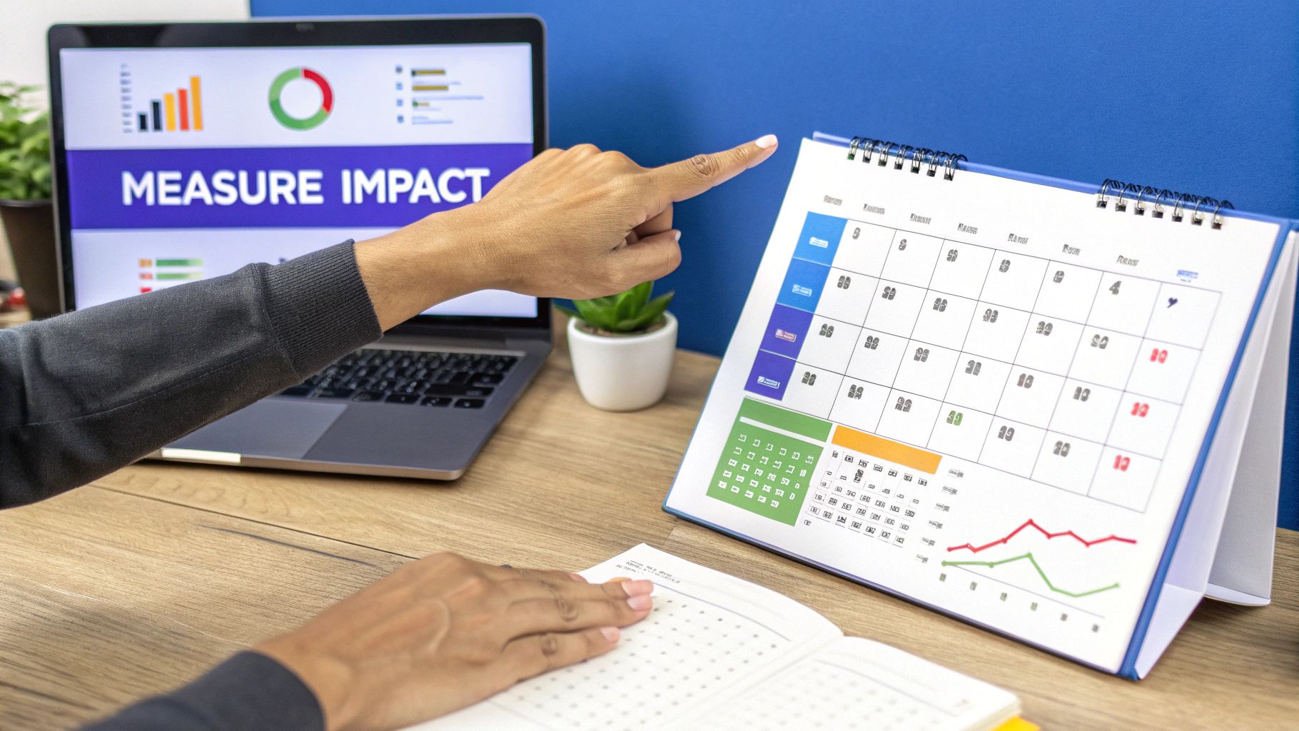 A person's hands on a desk, pointing at a calendar next to a laptop displaying 'MEASURE IMPACT' and graphs.