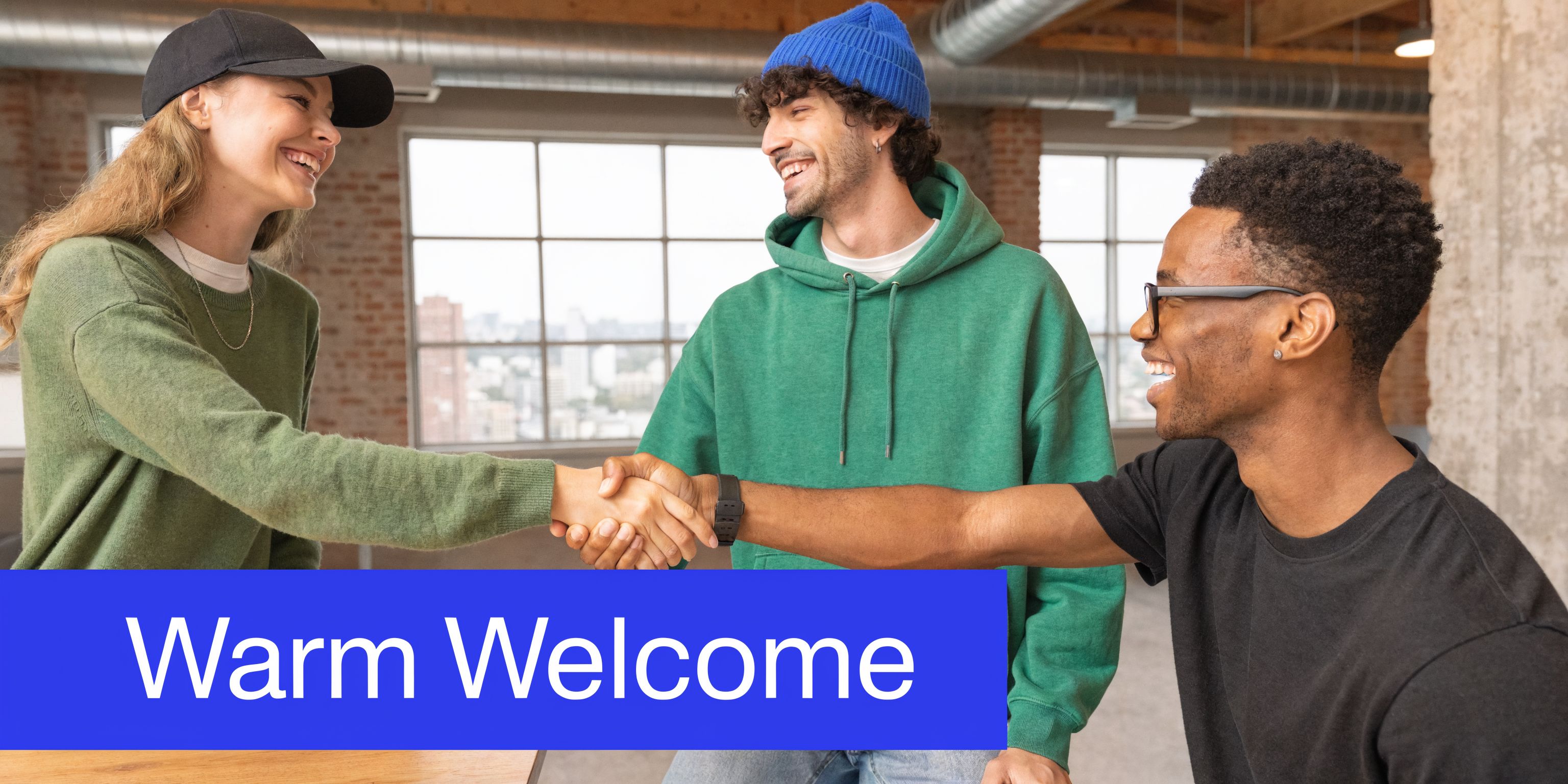 Three young, diverse professionals in a bright office laughing and shaking hands to welcome a new teammate.