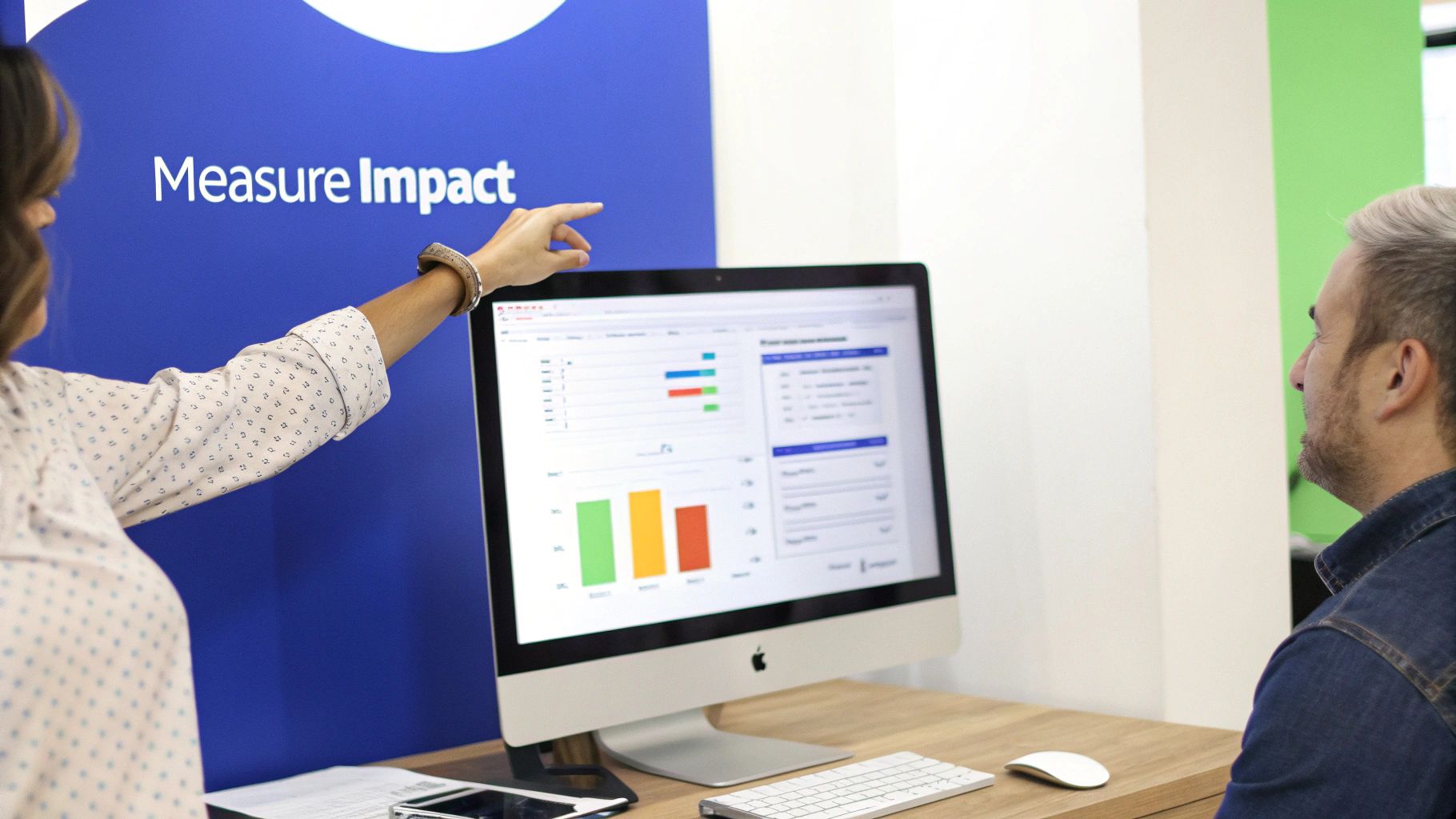 Two professionals discuss data analytics displayed on an Apple iMac computer screen in an office.