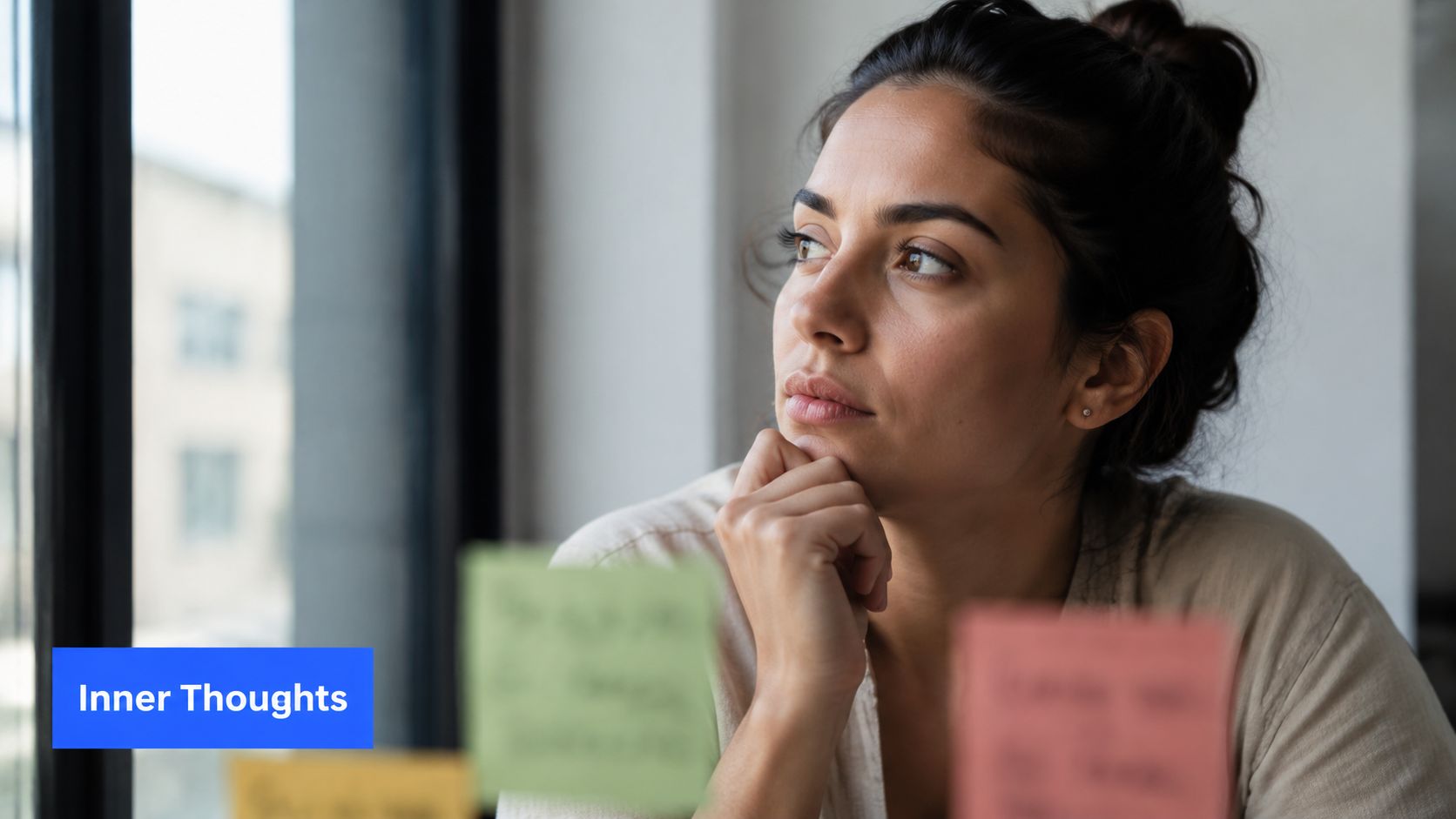 A thoughtful young woman looking out a window while contemplating ideas on colorful office sticky notes.